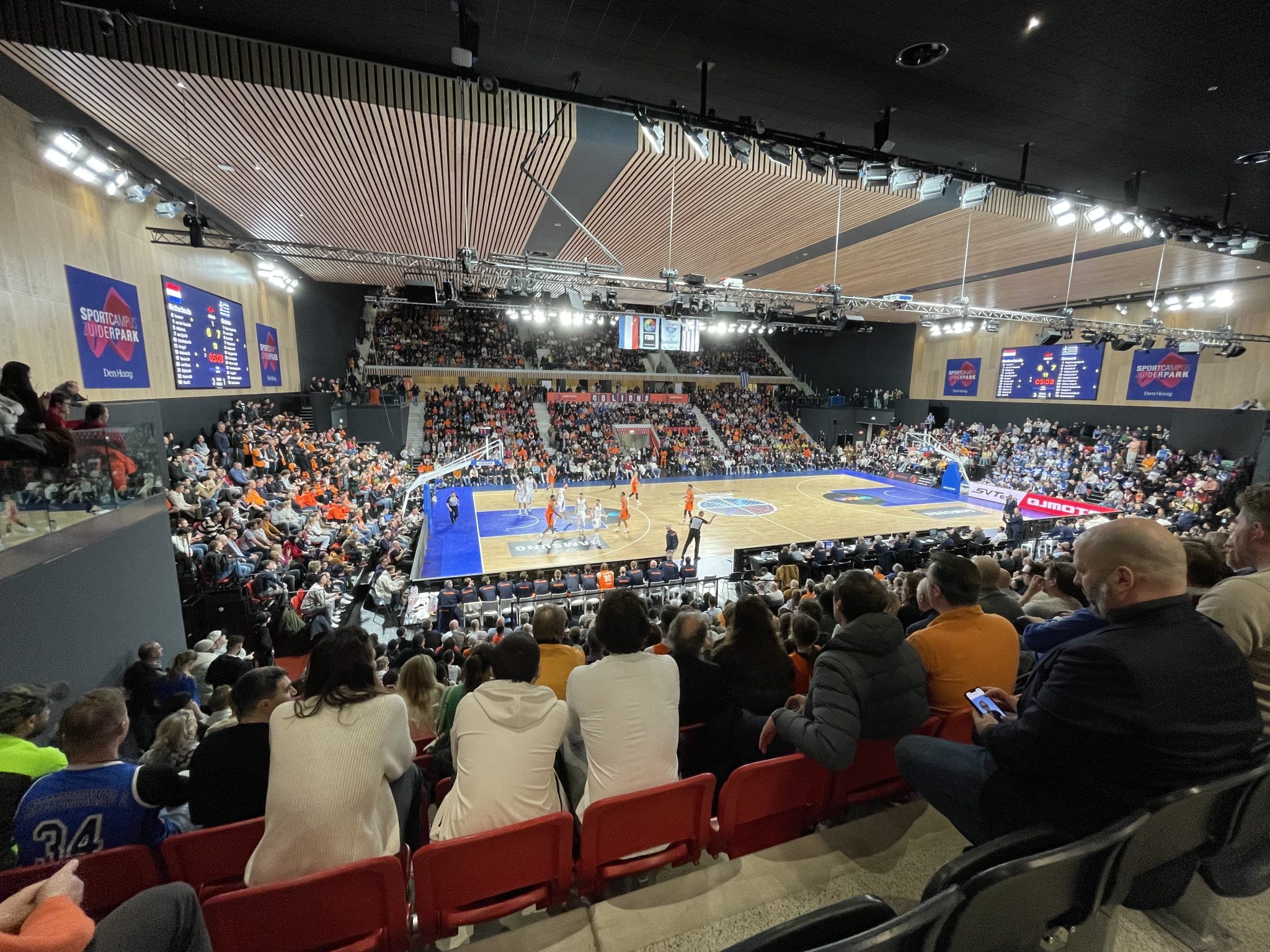 Volle tribunes in de topsporthal van Sportcampus Zuiderpark met het LED-scorebord boven het veld